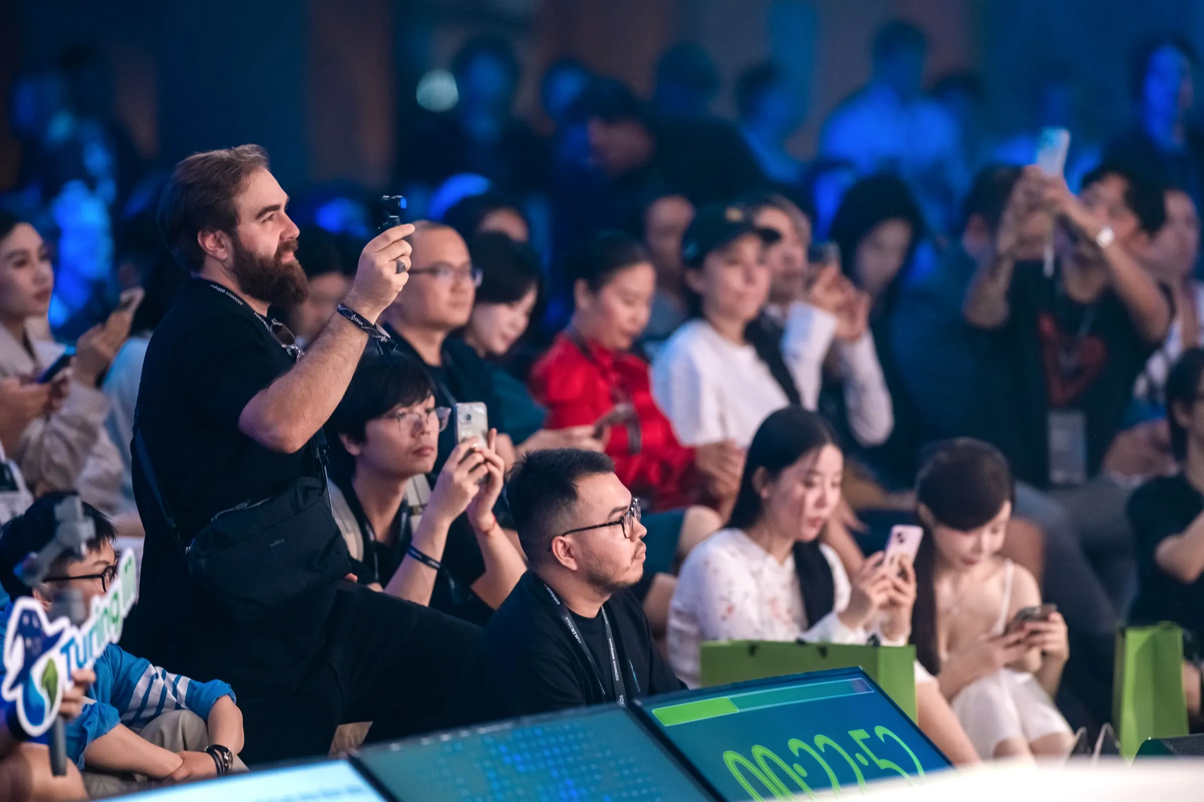 Audience packed shoulder to shoulder, phones raised and filming