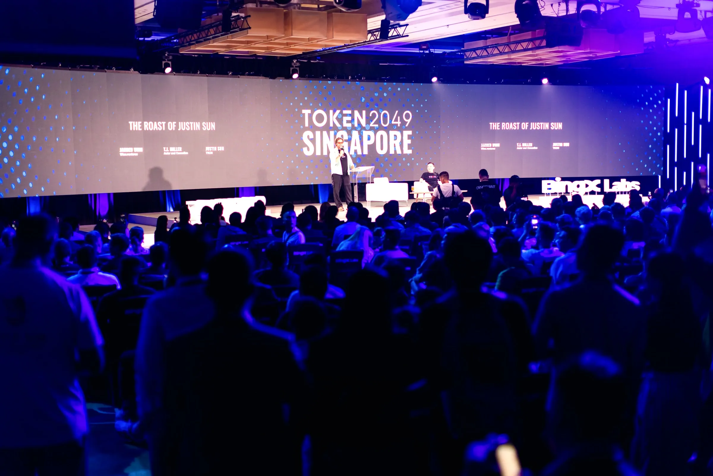 The Roast of Justin Sun: the room seen from the stage at Token2049 Singapore — every seat full, attendees seated in the aisles and standing at the back