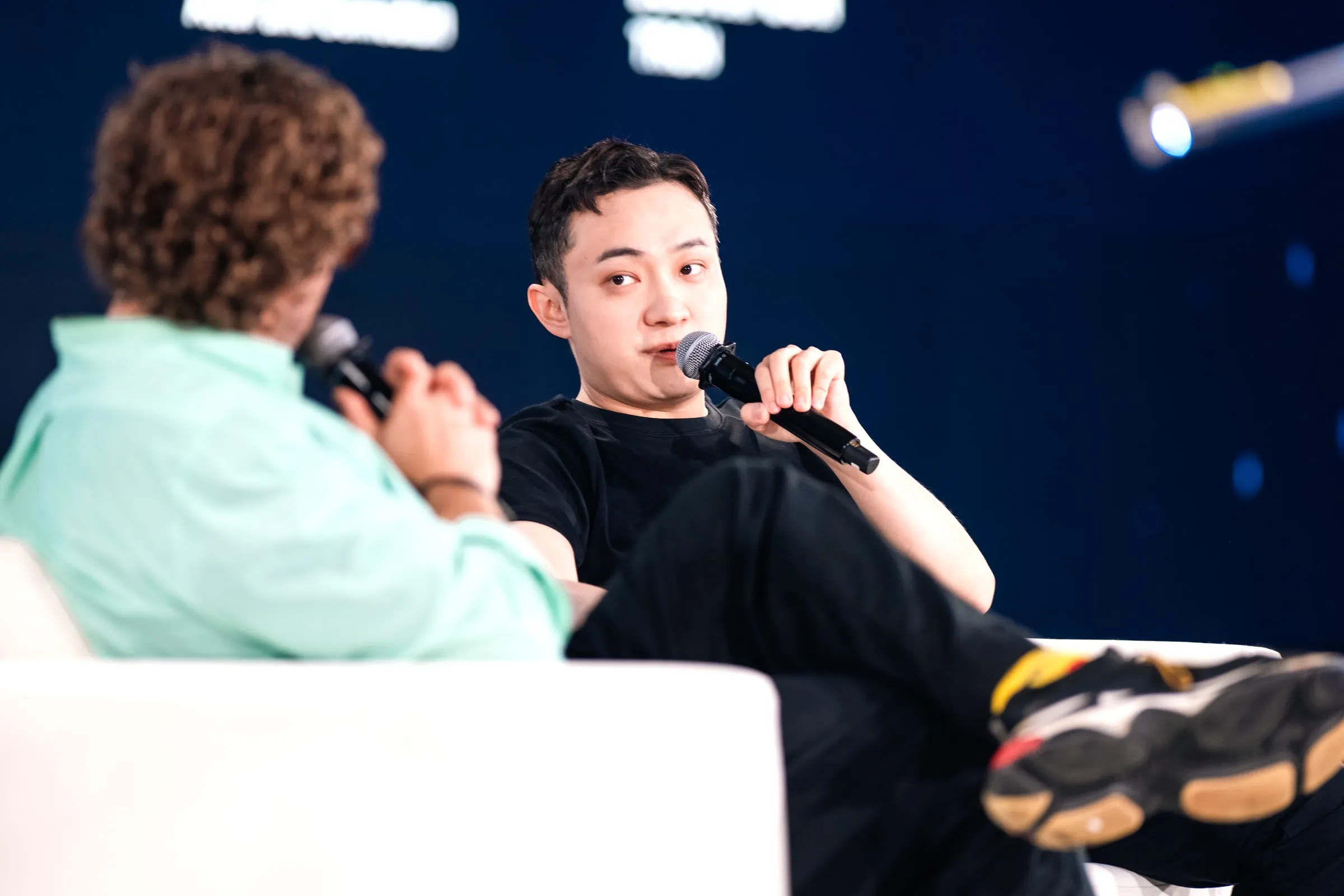 T.J. Miller and Justin Sun trading lines on stage, both holding microphones